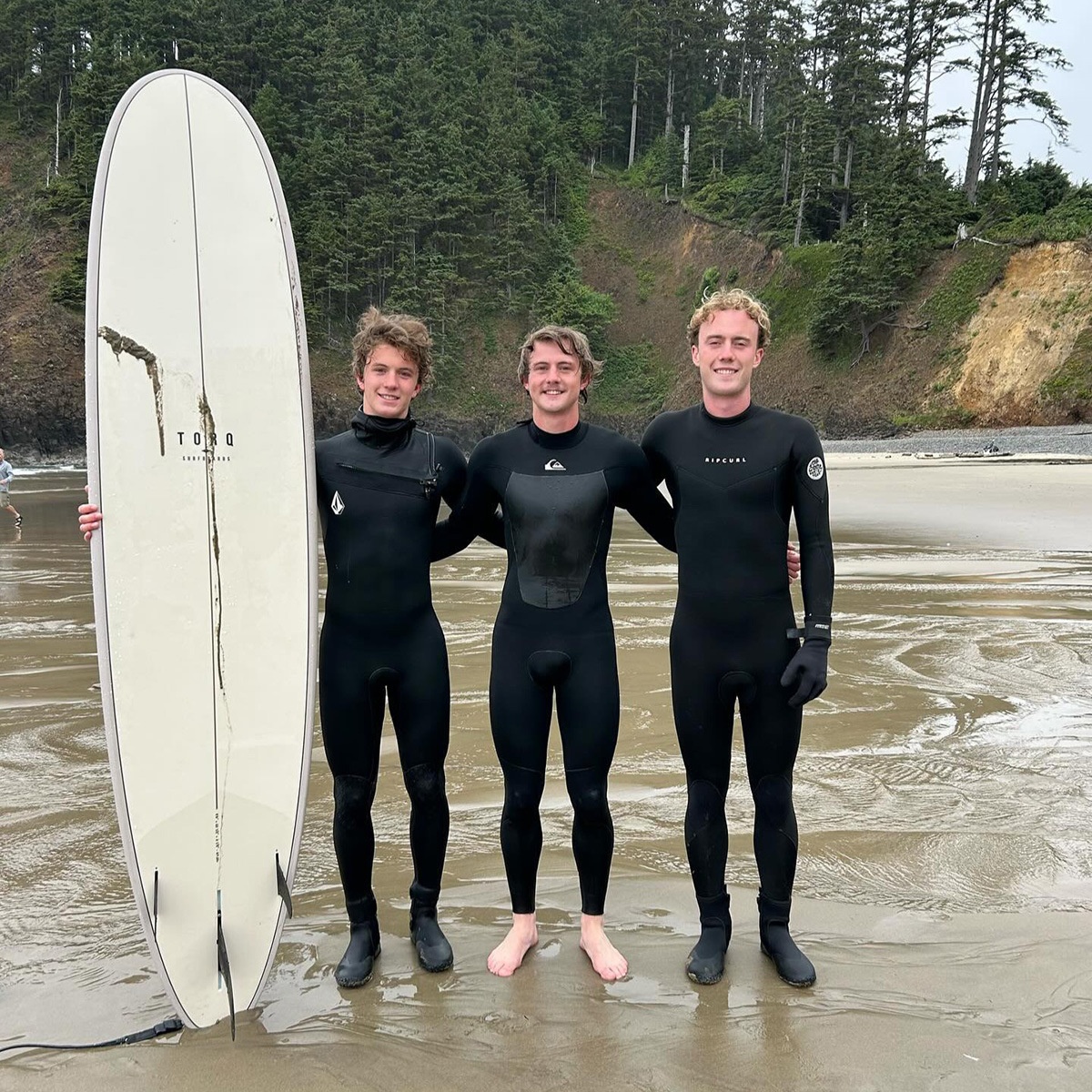 guys standing on indian beach oregon holding a torq surfboard in their wetsuits