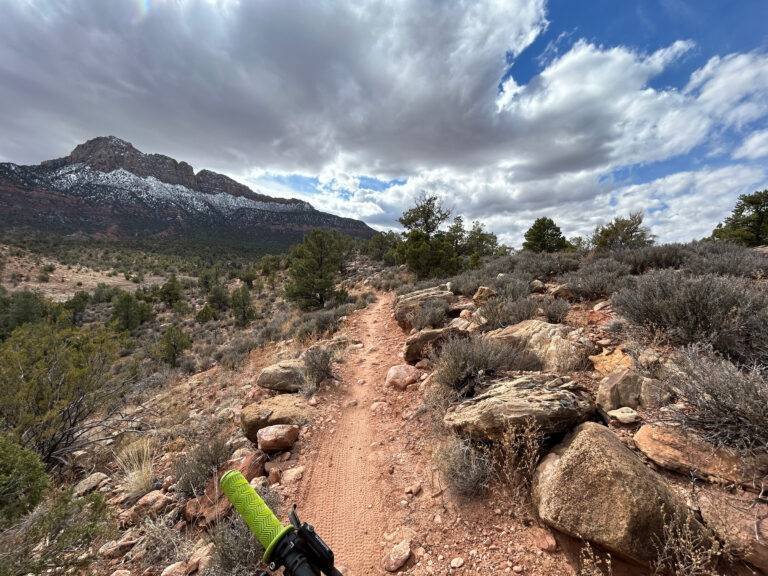 Riding singletrack on the Wire Mesa trail with a snow-capped peak in the distance